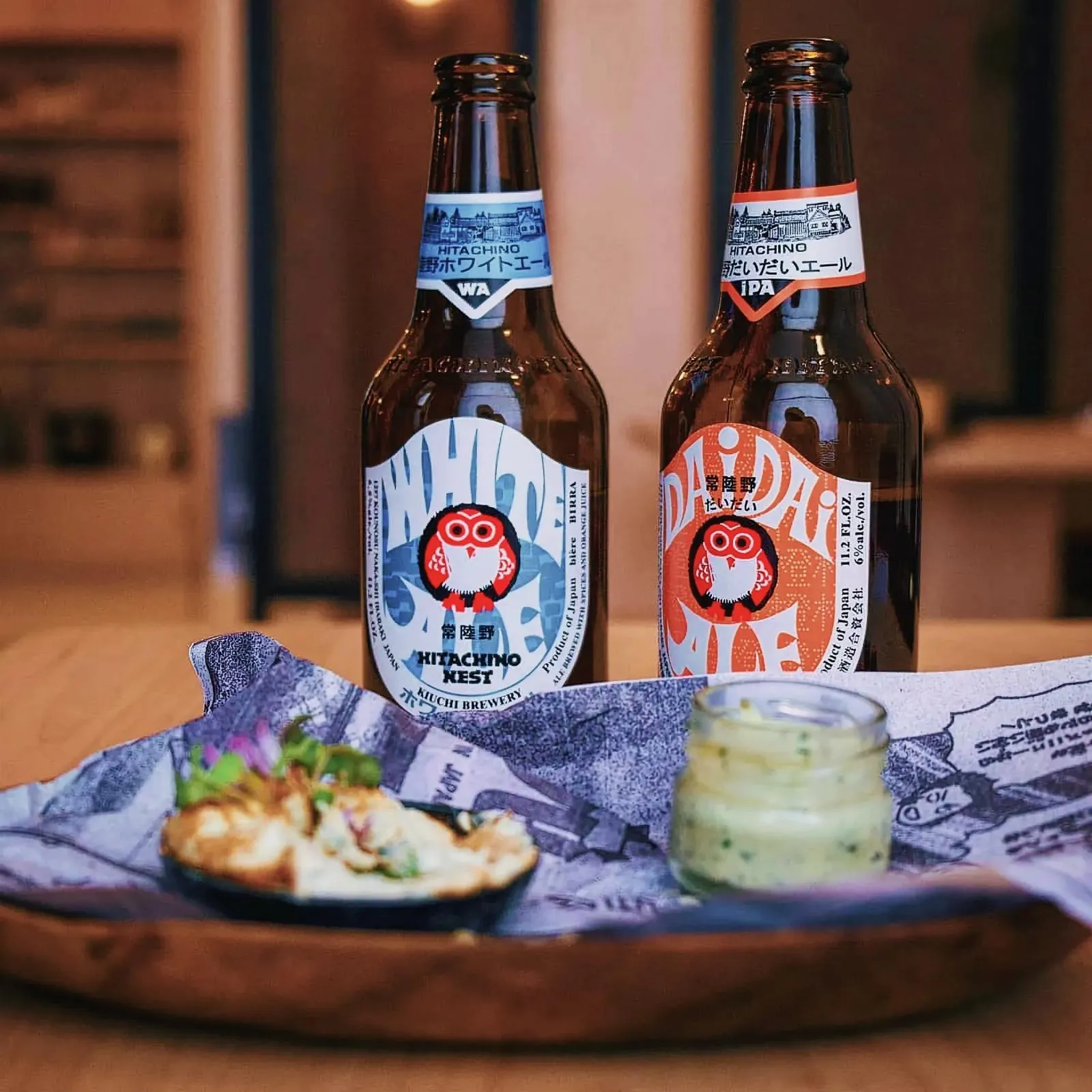Close-up of Hitachino Nest Beer bottles and plate of food on a wooden table.
