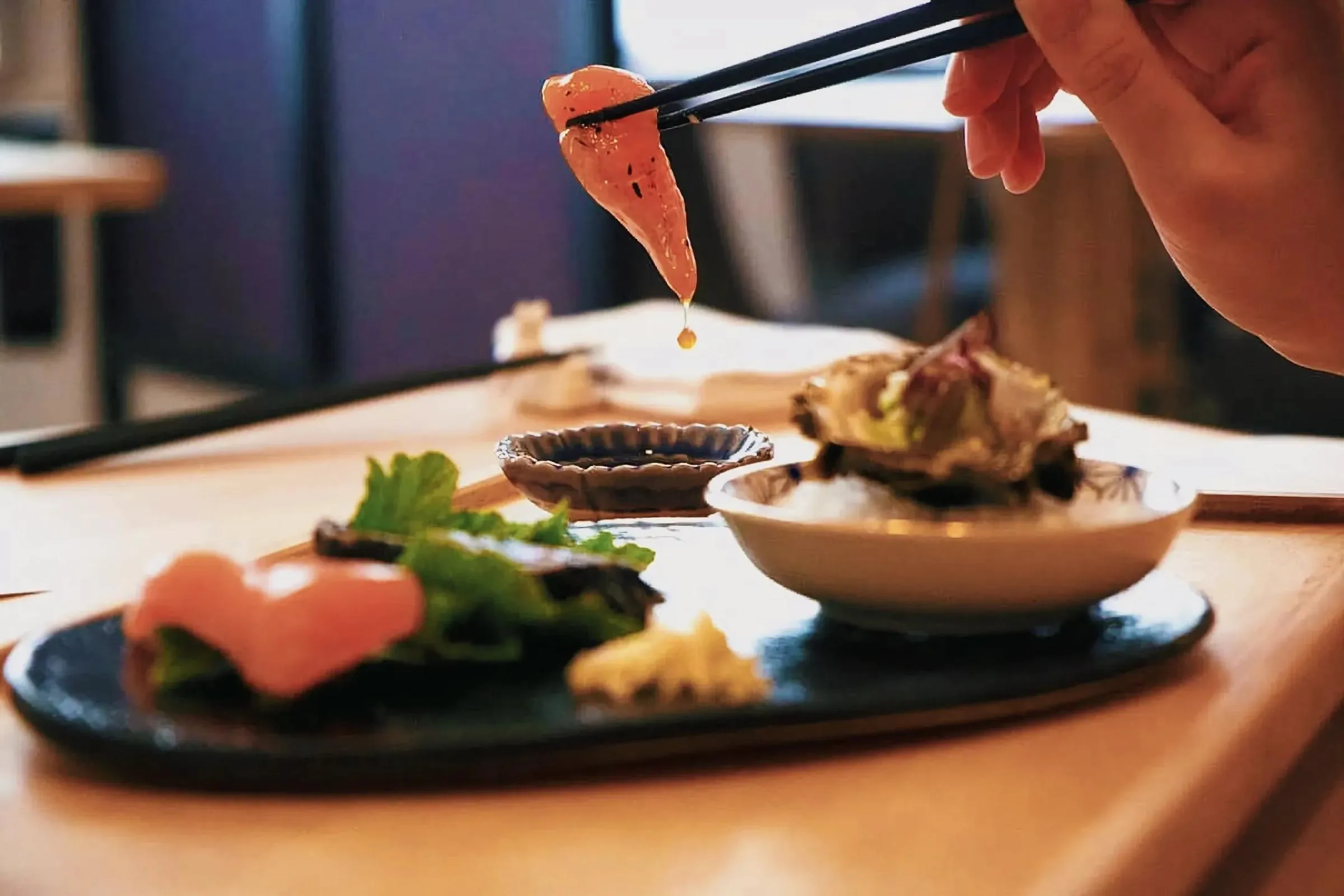 Person holding sushi with chopsticks at Tjing Tjing House