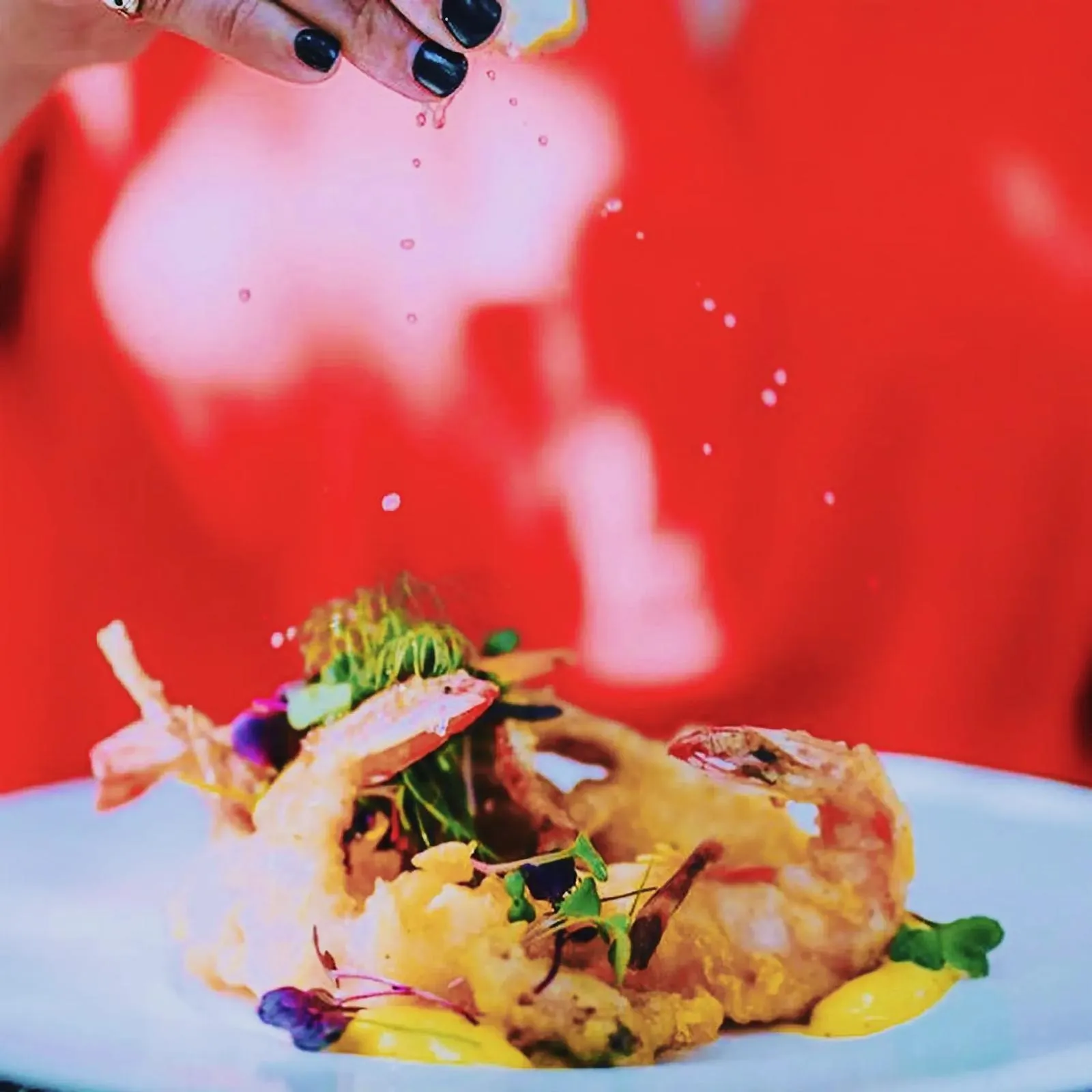 A person sprinkling salt onto a plate of seafood