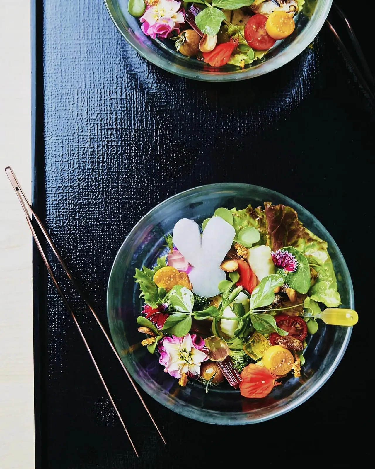 Table setup with a bowl of fresh salad, chopsticks, and a bunny-shaped object.